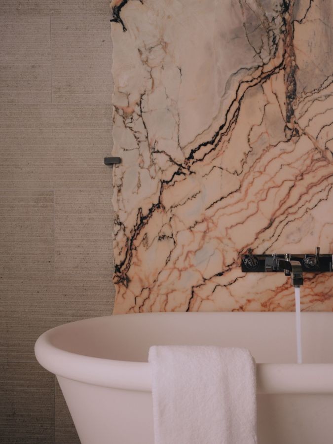 Freestanding bathtub on pink veined marble wall